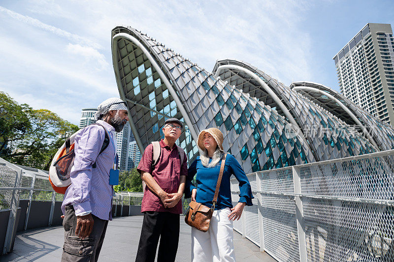 两名亚洲老年游客享受吉隆坡城市之旅，聆听当地导游讲解吉隆坡市中心萨洛玛桥的建筑和历史