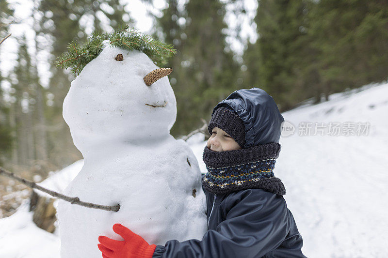 一个快乐的男孩和白雪公主在森林里玩耍。他穿着一件深色夹克，戴着红色手套。冬天,下雪了。库存图片
