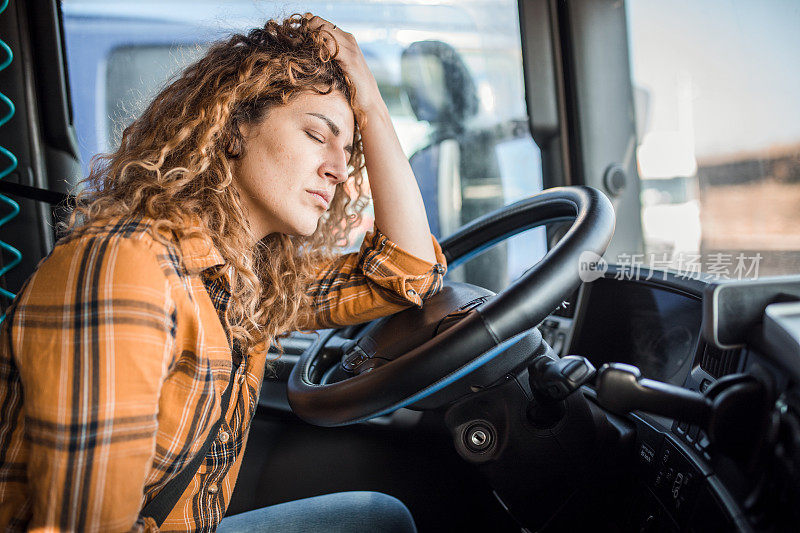 一个疲惫的卡车司机闭着眼睛抱着头坐在驾驶座上。她头痛，劳累不堪