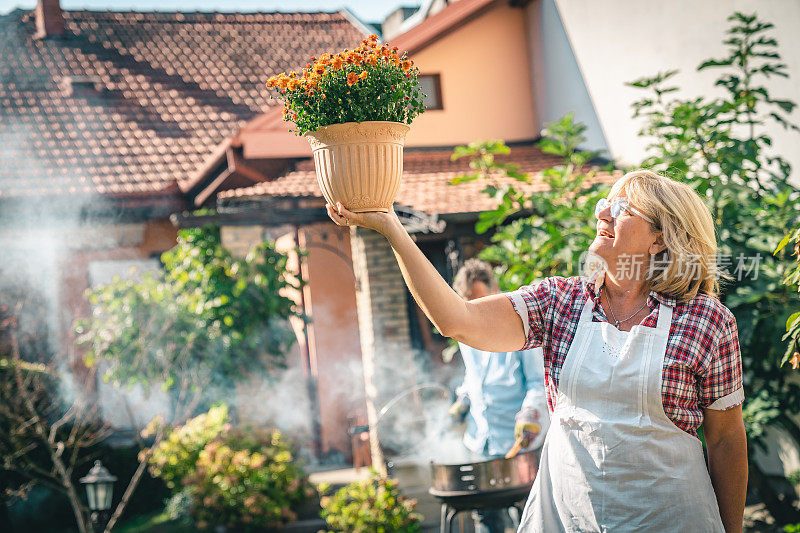 兴高采烈的老年妇女捧着一个花盆，欣赏着她那郁郁葱葱的植物
