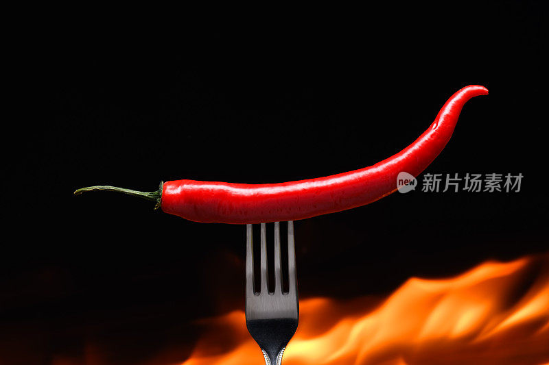 红辣椒，用叉子戳着，背景是燃烧的火，火焰在黑色的背景上