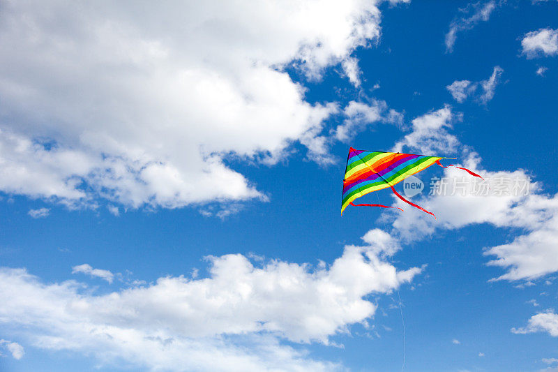 彩虹风筝在蓝色多云的天空中飞翔。