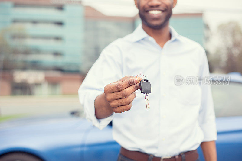 微笑的男人拿着车钥匙提供新的蓝色的车