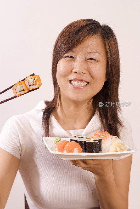 年轻的亚洲女孩与两个寿司Maki之间的筷子