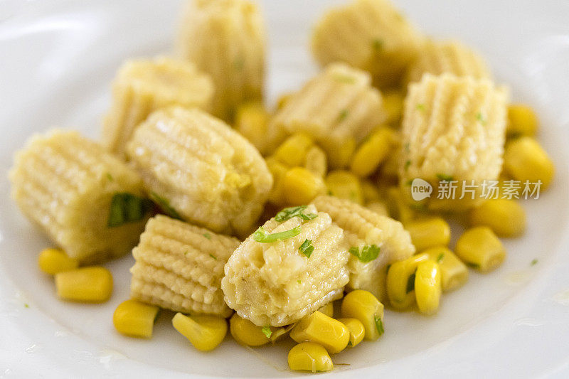 白色盘子上的玉米特写，里面有小玉米、玉米粒和一些欧芹。