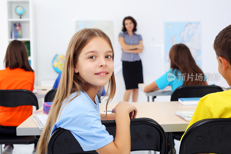 坐在教室里的小学生。微笑的女孩转向相机。