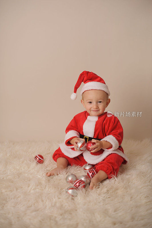 微笑的婴儿穿着圣诞老人服装玩圣诞饰品