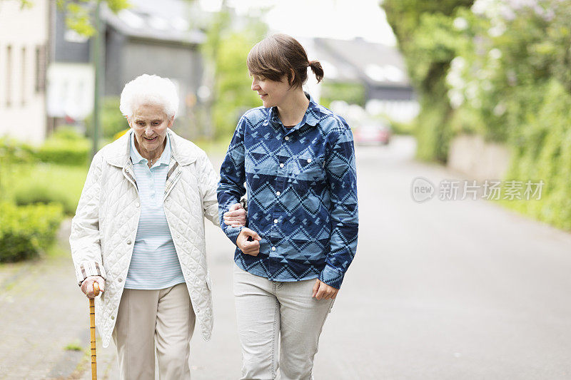 年轻的看护者帮助在街上行走的老年妇女