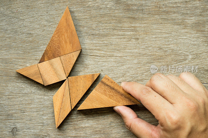 手握三角形完成蝴蝶形状的七巧板拼图(自由、自由生活或探索新世界的概念)