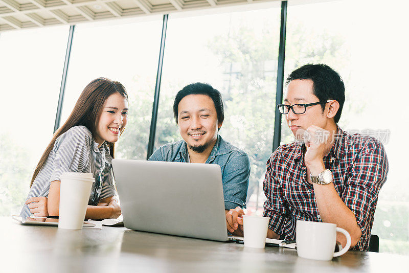一群年轻的亚洲商业同事或大学生在咖啡馆或现代办公室使用笔记本电脑进行团队非正式讨论，启动项目会议或愉快的团队头脑风暴概念