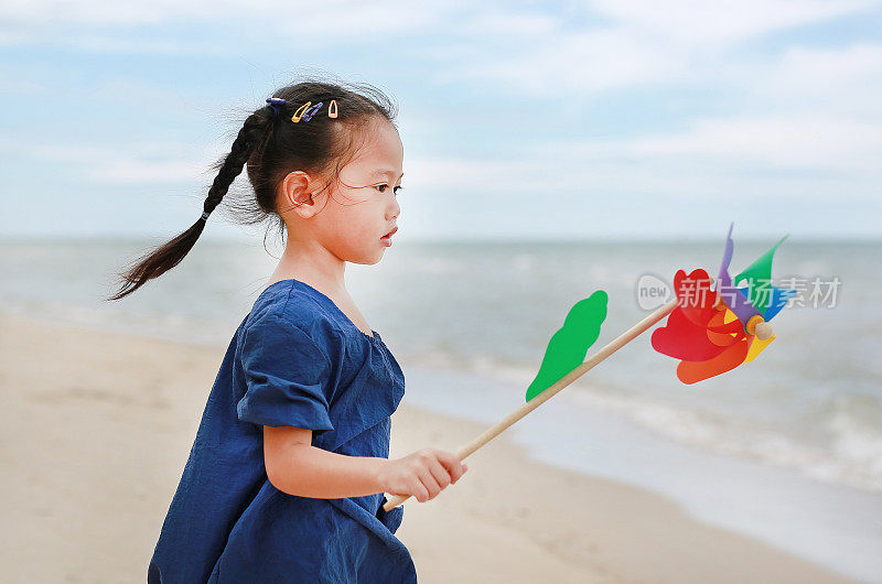 快乐的小女孩手拿风车在海边望着大海。