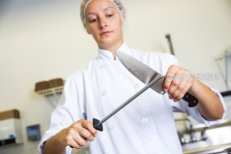 一个受过专业训练的厨师在一个商业厨房的工作台上磨刀