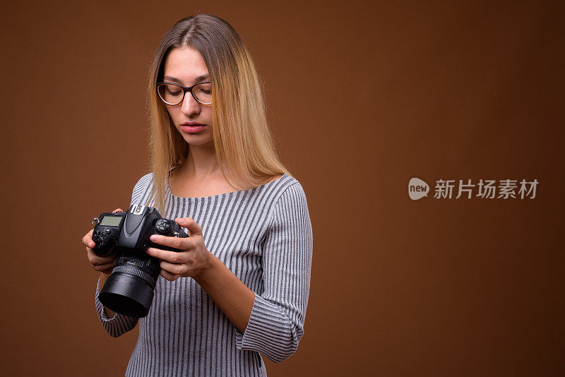 工作室拍摄的年轻美丽的女子与相机穿着灰色长袖衬衫，以彩色背景