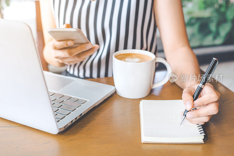 商务女性的手是写钢笔、笔记本和在办公室使用电话。