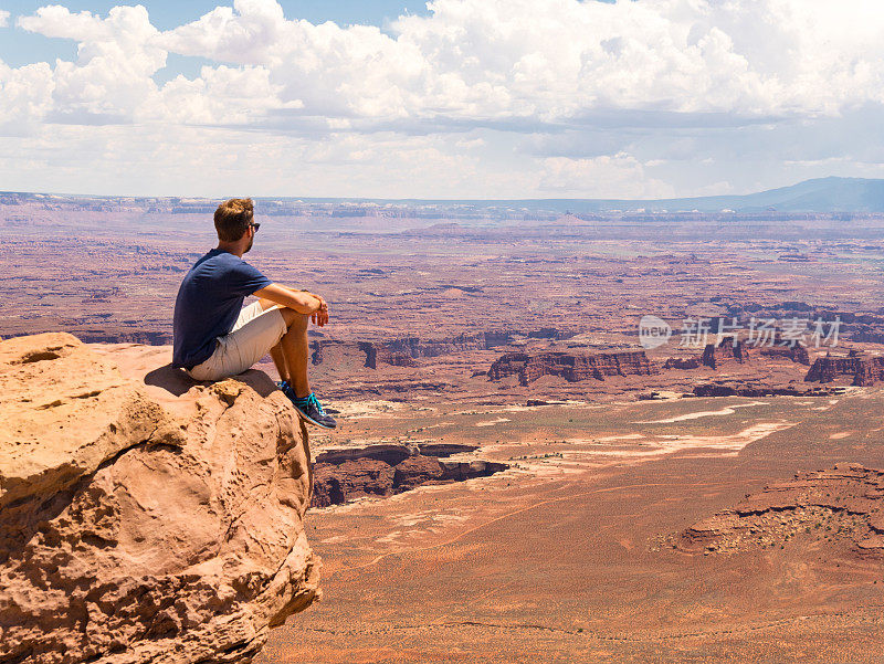 年轻人坐在悬崖上峡谷地国家公园，摩押，犹他州