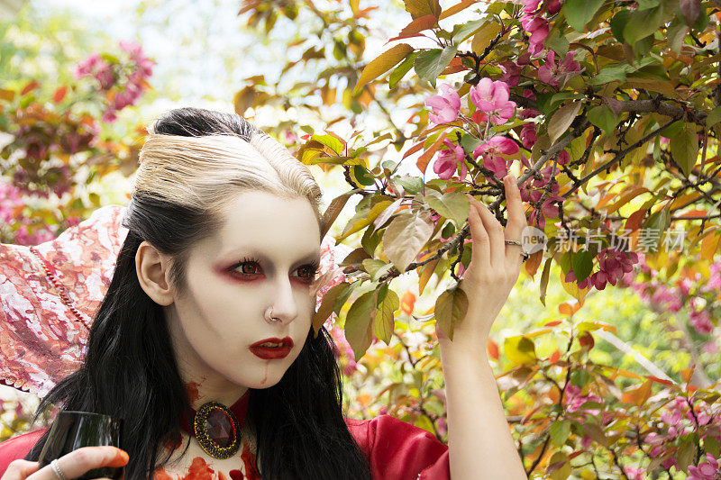 年轻女子在吸血鬼化妆，头部和肩部，与深粉红色的春天花朵。