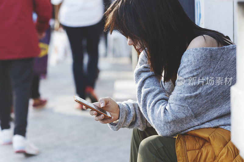年轻女子坐在靠近临街门的地方，使用智能手机