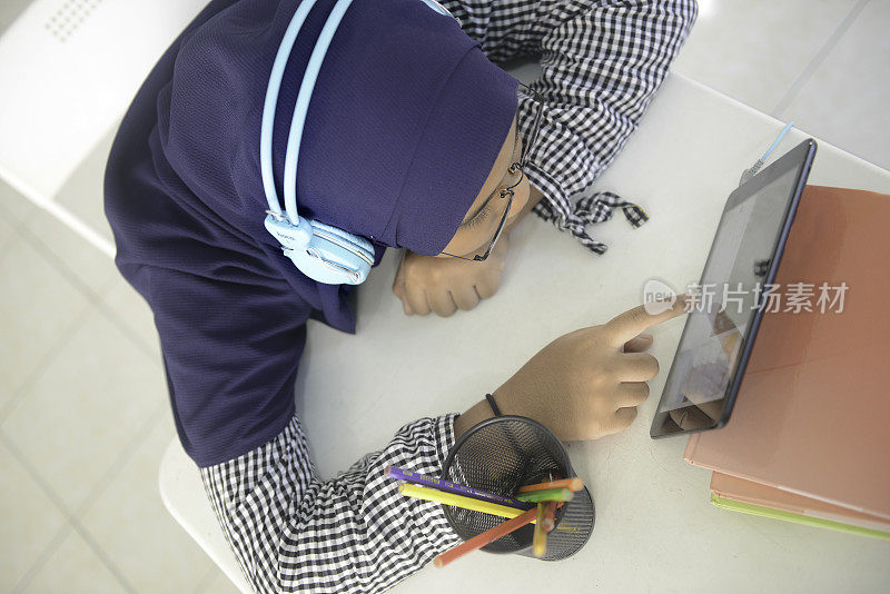 亚洲少女戴着耳机用平板电脑做作业