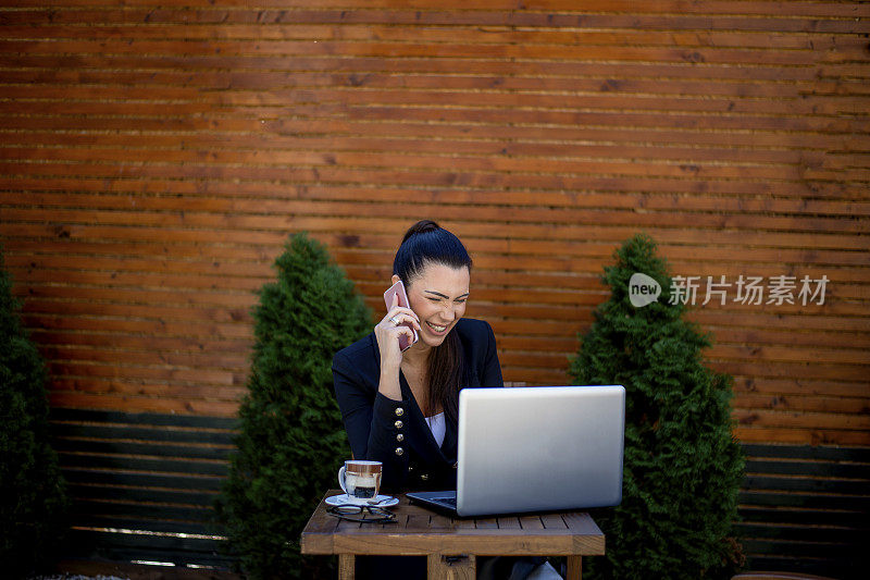 微笑的女商人用手机在咖啡店用笔记本电脑工作