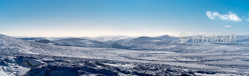 全景寒冷的野生景观覆盖在积雪在冬天遥远的山脉和朦胧的阳光和蓝天