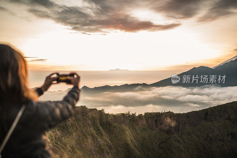 一位女士在山上用手机拍摄日落