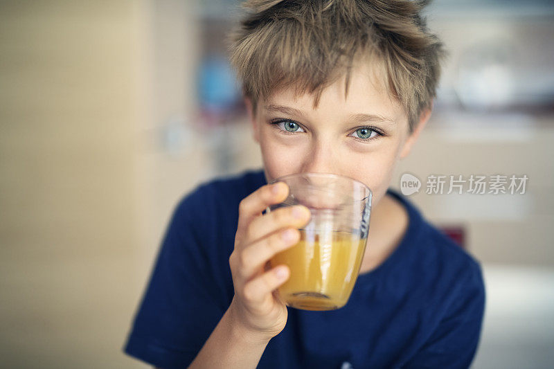 可爱的小男孩喝着一杯橙汁