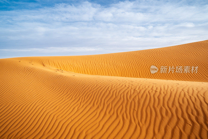 巨大的橙色沙状沙丘和多云的天空在Merzouga沙漠，摩洛哥。