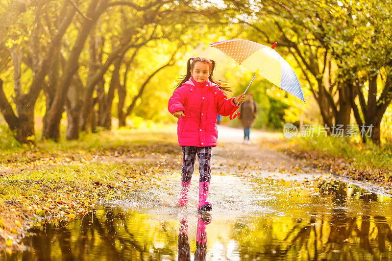 快乐的小女孩在雨中撑着伞跑过水坑