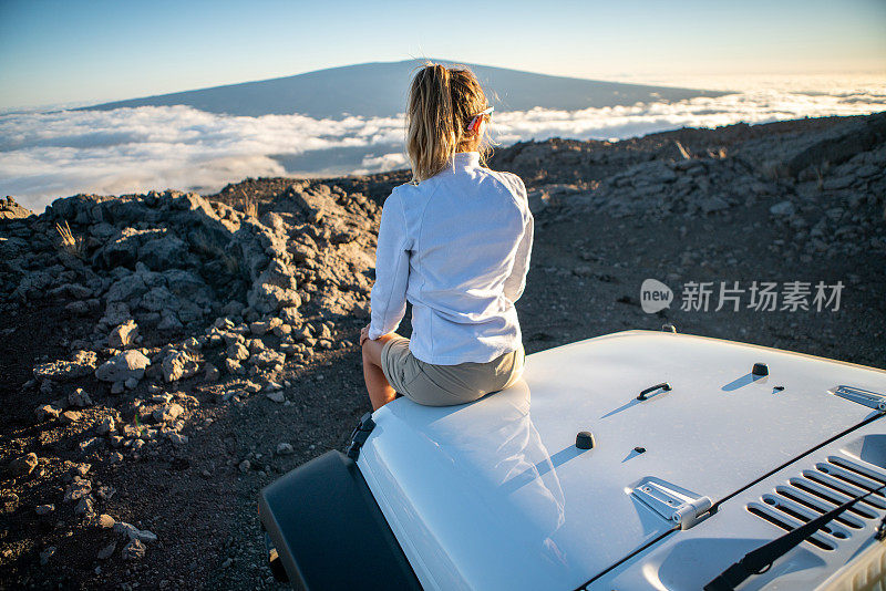 年轻女子坐在4x4引擎盖车看火山，在云端