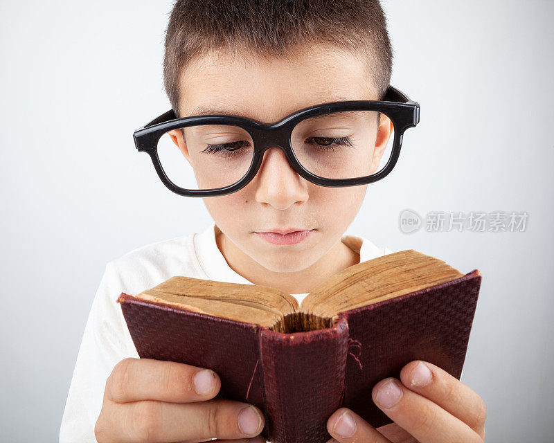 书呆子小男孩戴着大眼镜读一本迷你书