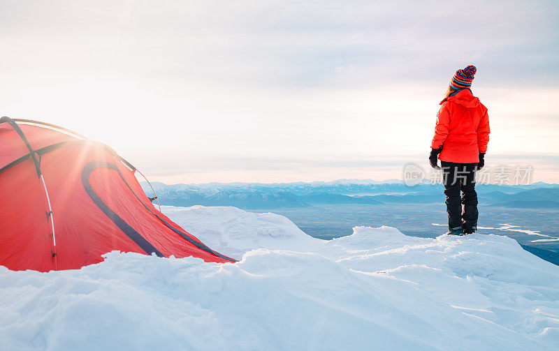 女性登山者正在看远处的露营帐篷在一个高海拔的山峰的顶峰