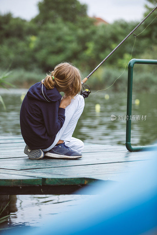 一个十来岁的小男孩蹲在河边钓鱼。