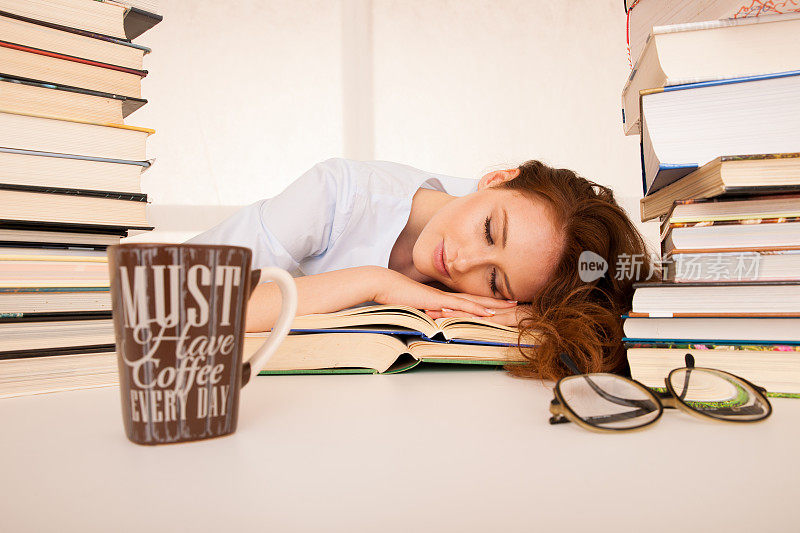 漂亮又疲倦的学生睡在一堆书上，桌上放着一个咖啡杯