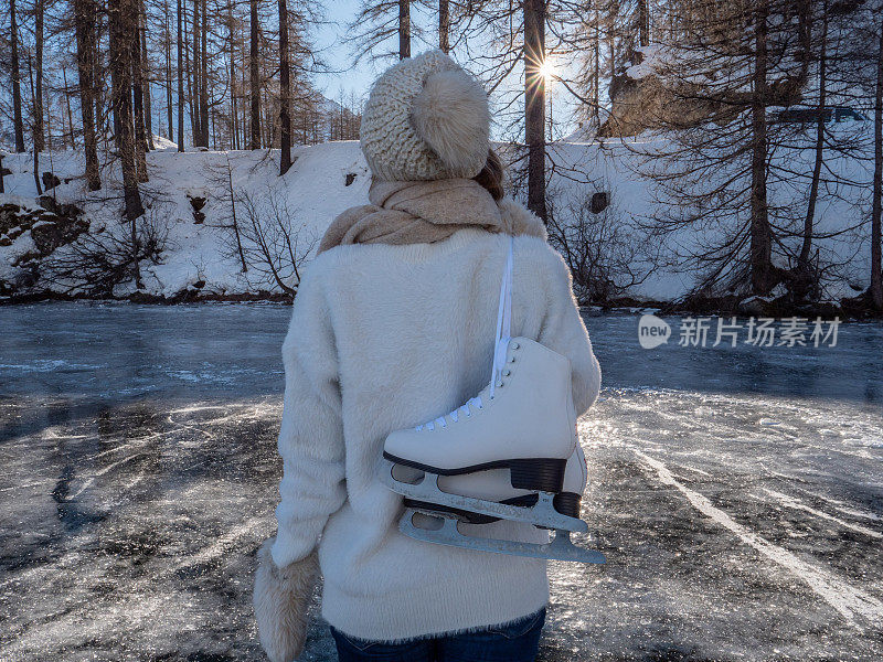 一个年轻女子肩上扛着冰鞋走在结冰的湖面上