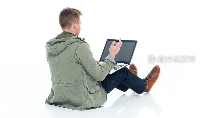 白人男孩坐在地板上，在白色的背景穿着纽扣衬衫和使用电脑
