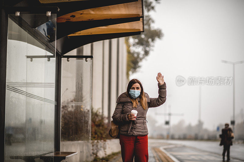年轻女子戴着防护口罩去上班。在公共汽车站停出租车