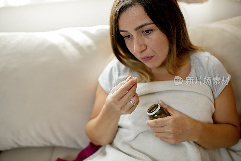 患流感的妇女在客厅的沙发上盖着毯子吃药