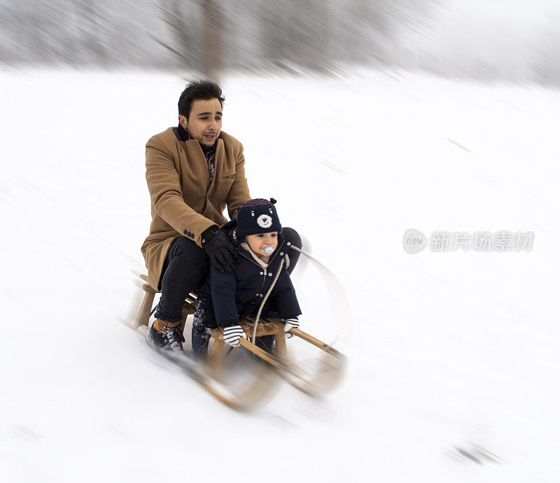 一个孩子和他的父亲坐着雪橇从雪坡上滑下来