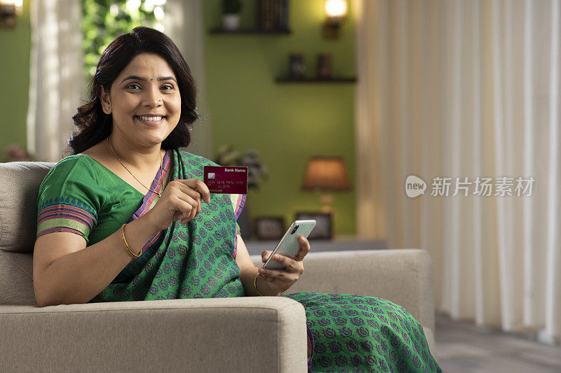美丽的印度女人用智能手机和信用卡在家网上购物，库存照片