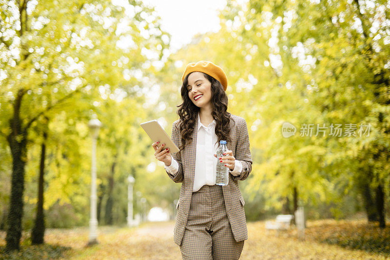 在她的数字平板电脑上喝水和阅读电子书的活力女人