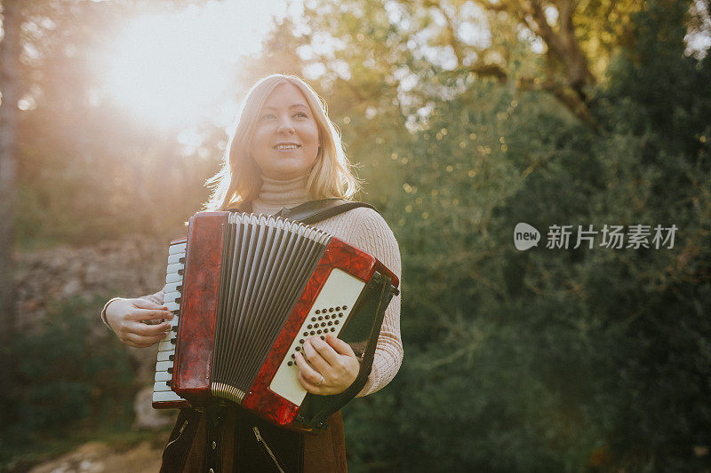 美丽的年轻女子在森林里拉手风琴