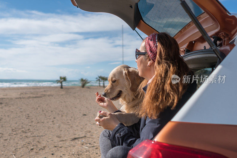 快乐的女人和她的狗坐在汽车后备箱里。