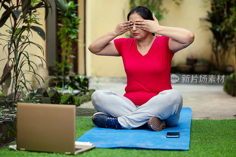 在线健身训练，资深女性在家用笔记本做瑜伽。