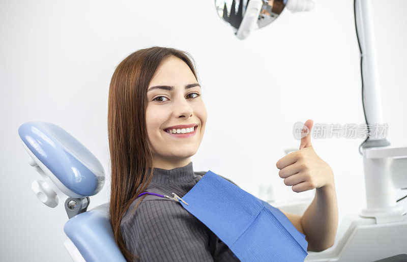 一位牙齿洁白、笑容灿烂的年轻女子坐在牙科诊疗室的椅子上。