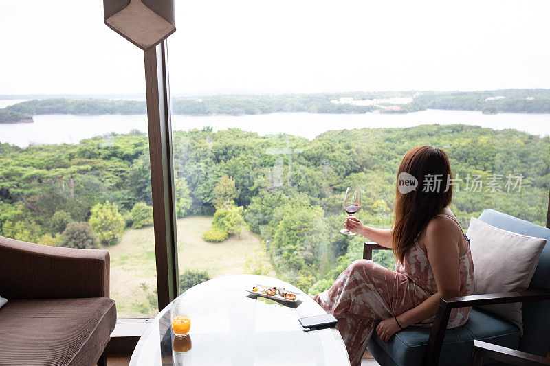 一个度假的女人靠窗放松，喝着酒欣赏风景