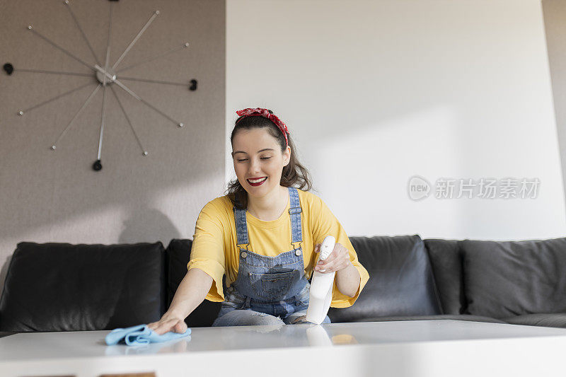 快乐的年轻女人用喷雾剂和抹布打扫房间