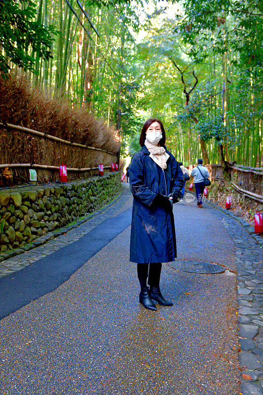 日本妇女走在路旁的茂密的竹林，佐野，京都