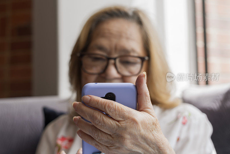 奶奶在家里的沙发上用手机和她的朋友和家人通过视频通话