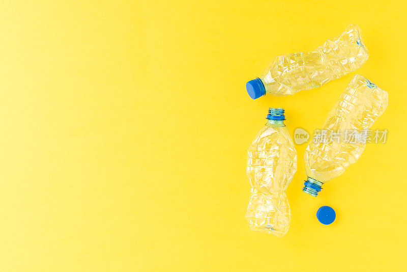 黄色背景上是空的和压碎的水瓶。塑料回收的概念
