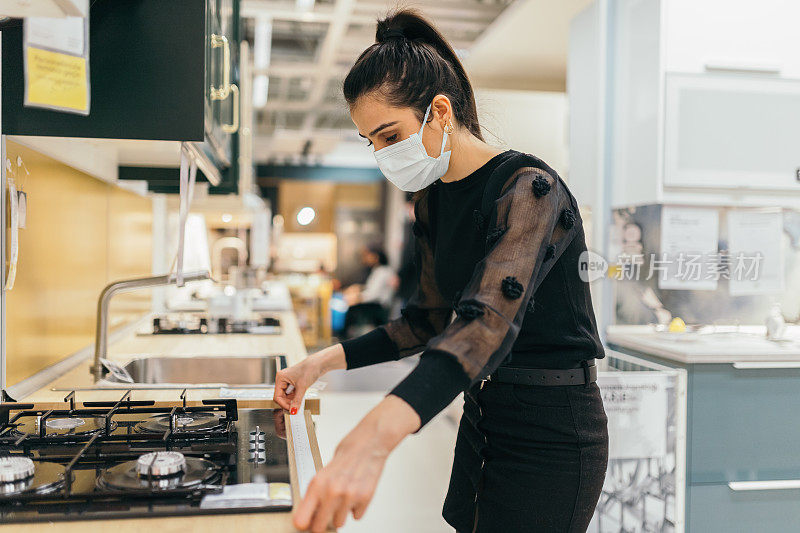 一位年轻女子在家具店购物时正在测量一件家具的尺寸